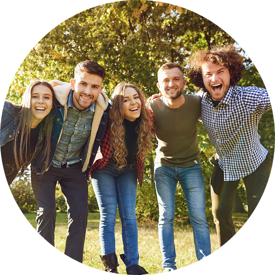 A group of young men and women are all standing outside with their arms around one another. They are smiling and laughing, all of them are enjoying life after treatment for addiction at Juniper Grove Recovery