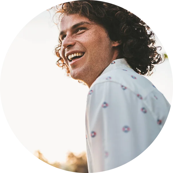 A young man smiles widely while standing outside at sunset. He is enjoying life after addiction treatment at Juniper Grove Recovery.