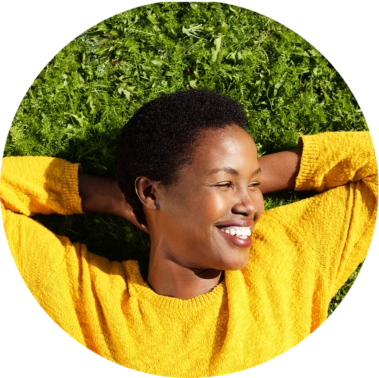 A woman lays in the grass with her hands clasped behind her head. She smiles brightly, enjoying life after addiction treatment at Juniper Grove Recovery.