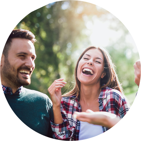 A young man and a young woman are sitting outside and laughing. They're enjoying life after addiction treatment at Juniper Grove Recovery.