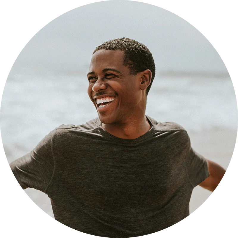 A man, standing lakeside, smiles broadly with his arms stretched wide. He is enjoying life after addiction treatment at Juniper Grove Recovery.
